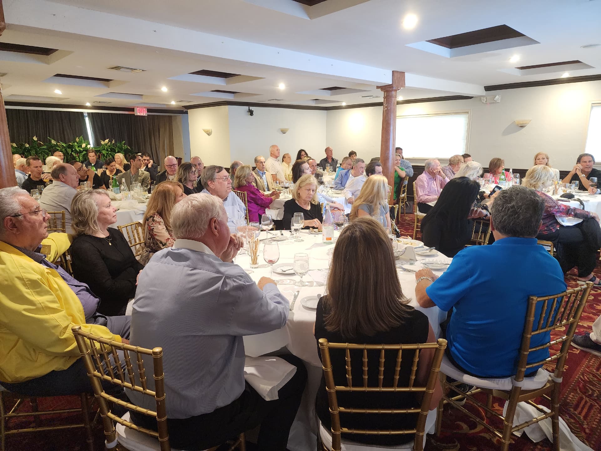 A full banquet room of guests at round tables watching a presentation