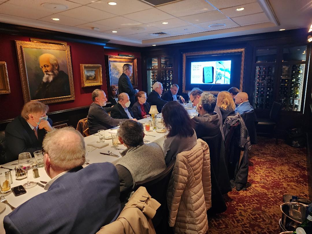 Guests seated at a long table in a wine-cellar dining room watching a product slide