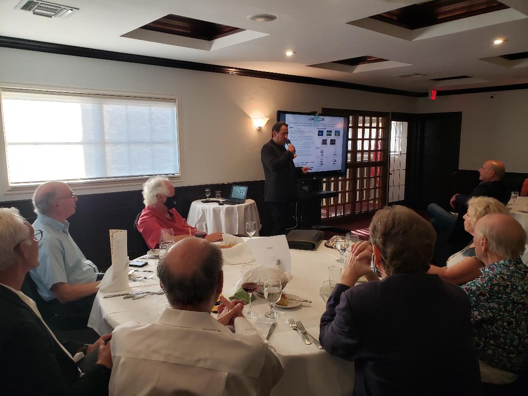 A speaker with a microphone presenting to guests around a dining table