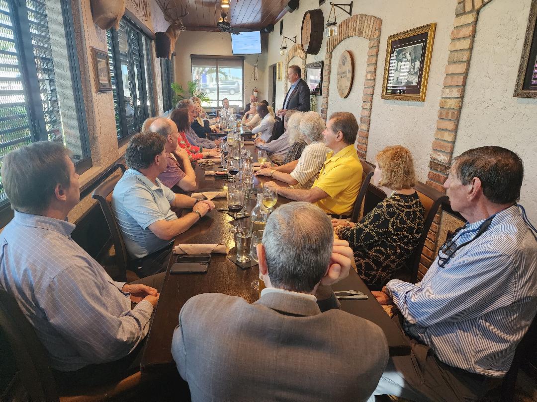 Guests at a long wooden table listening to a presenter in a rustic dining room