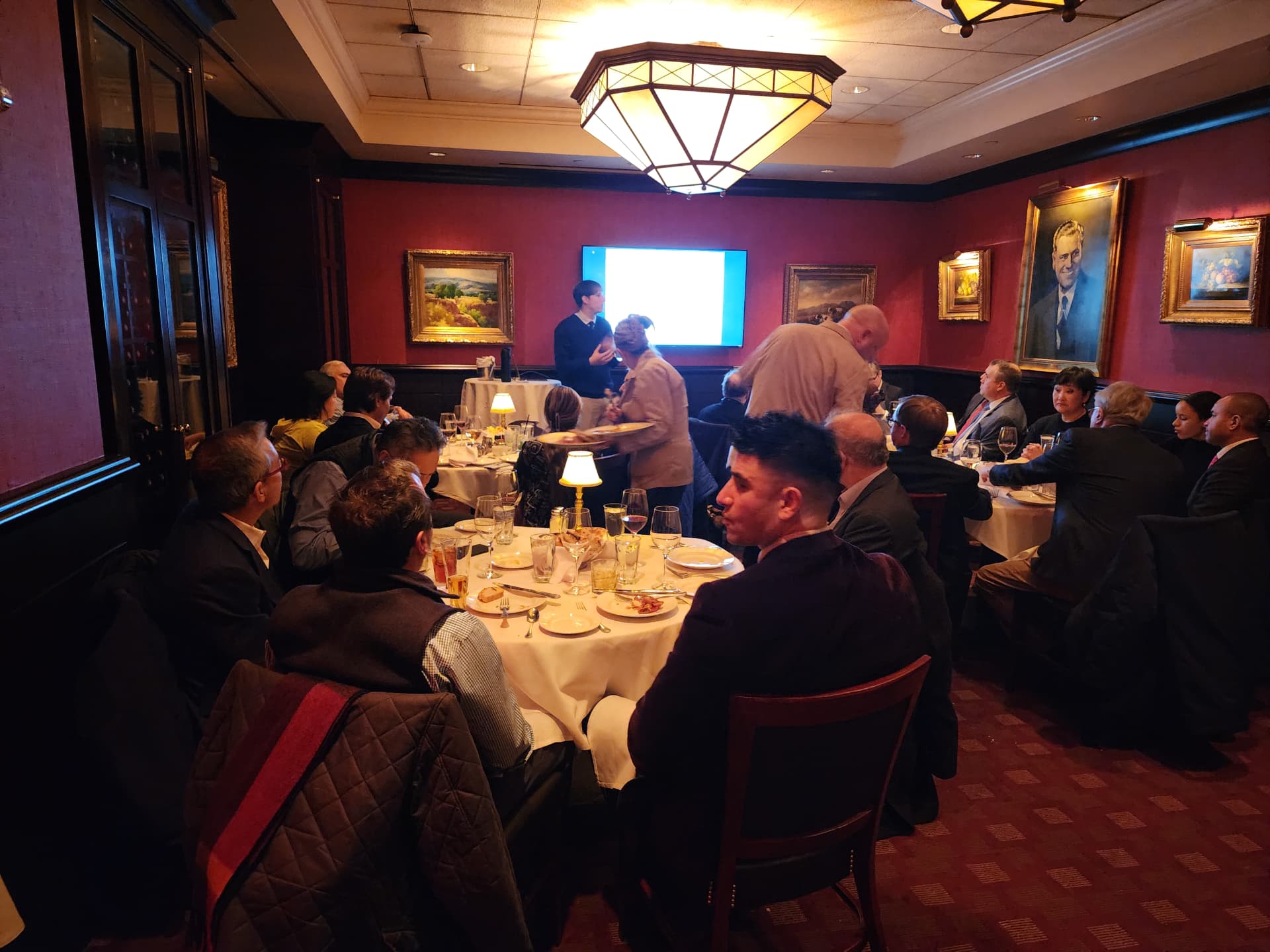 Guests dining in a red-walled private room while a presentation continues on screen