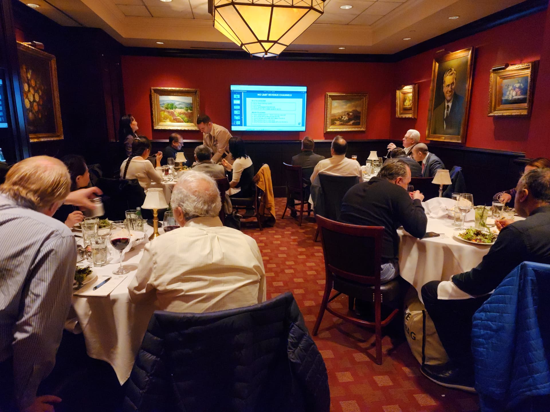 A presenter reviewing a revenue-channel slide with guests at a private dinner
