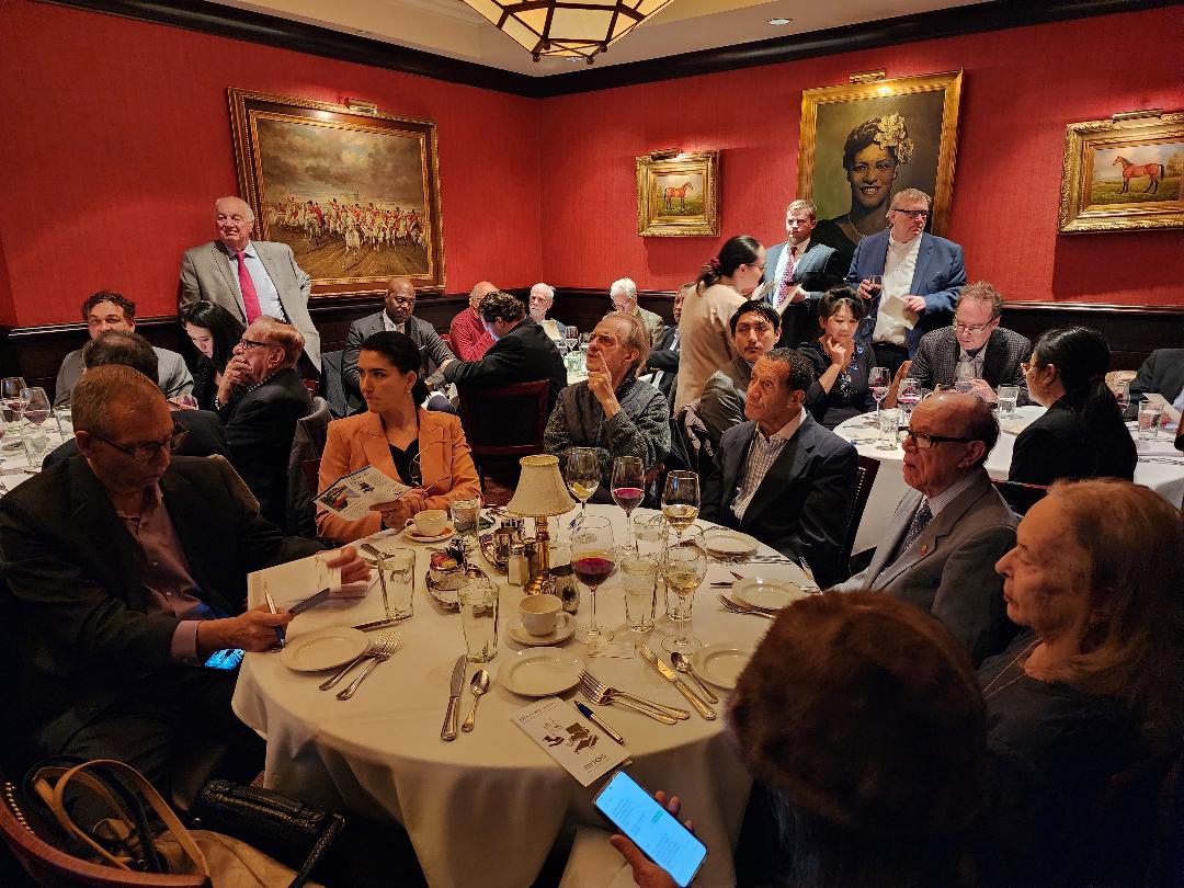 A full red-walled dining room of guests during an investor presentation