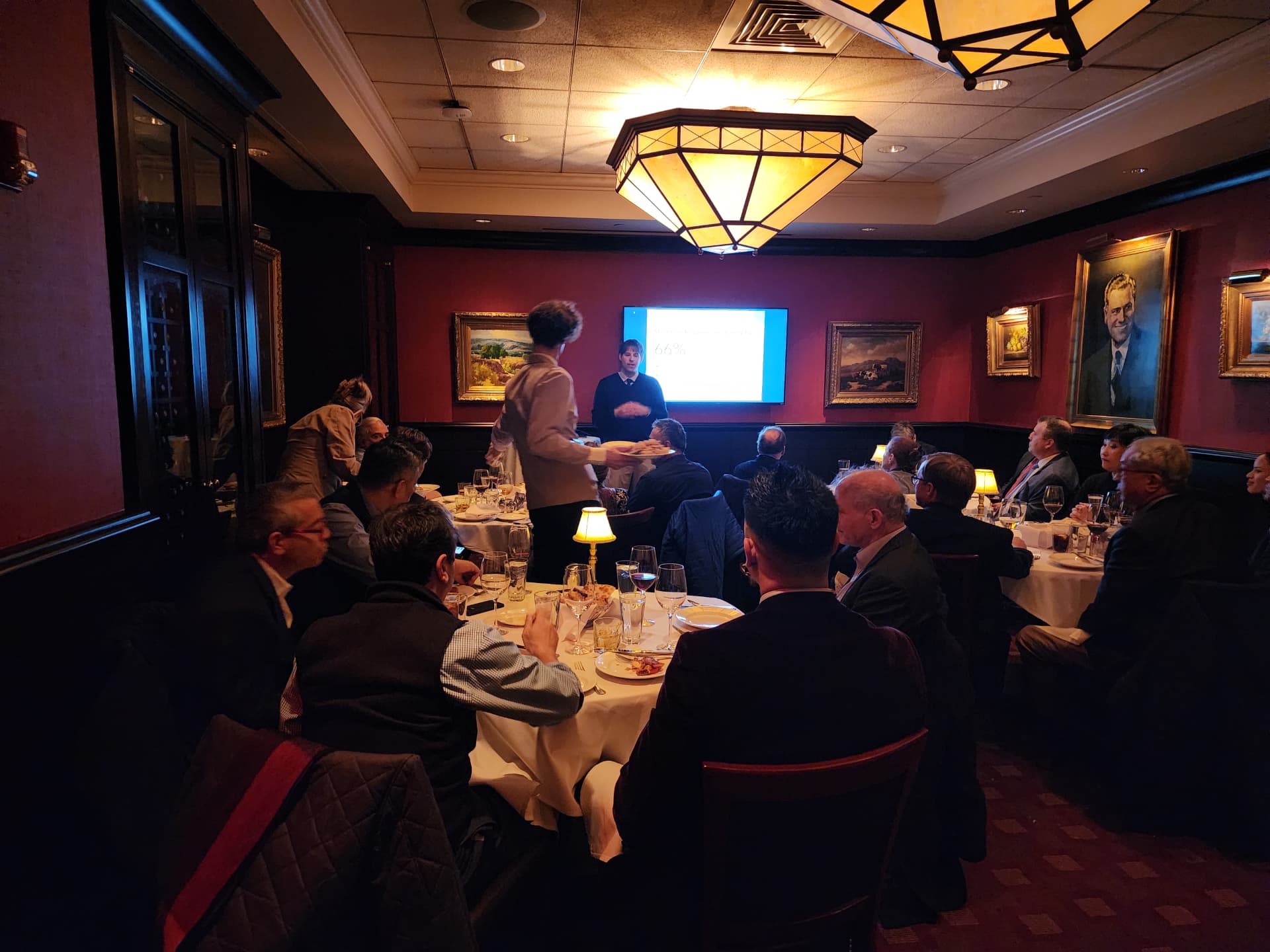 Servers delivering courses as a presenter shares results in a red dining room