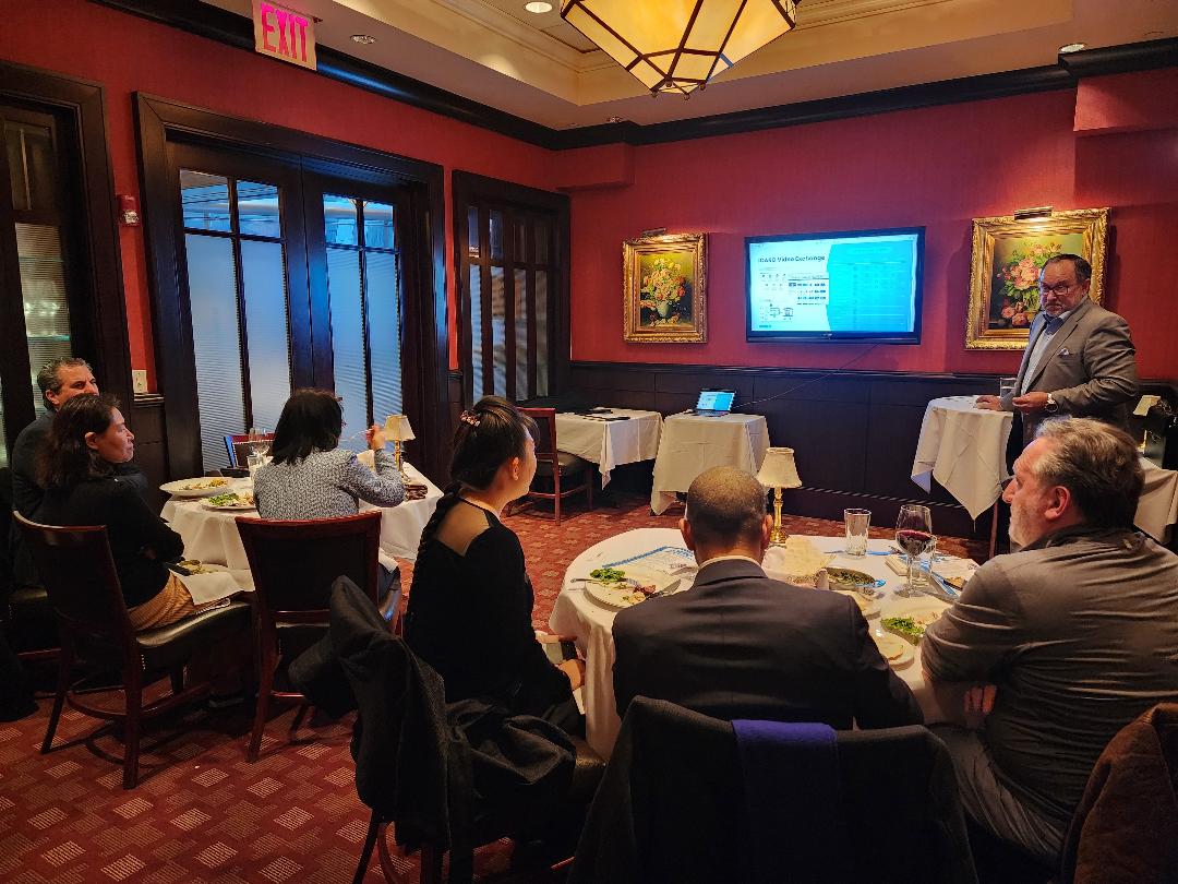 A presenter addressing guests in a red-walled private dining room with a data slide on screen