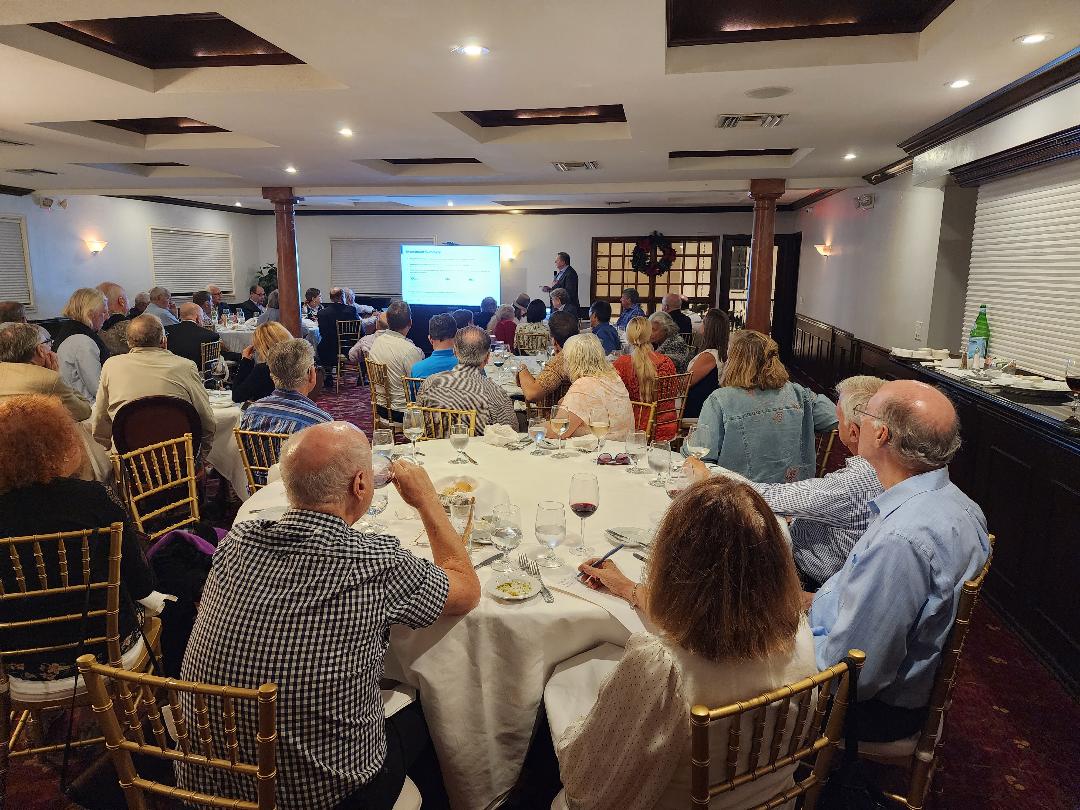 A large banquet room of guests watching a presenter beside a projected summary slide