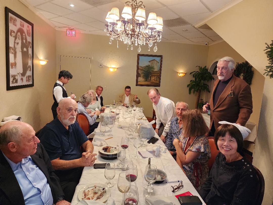 Guests along a chandelier-lit long table after dinner at a private presentation