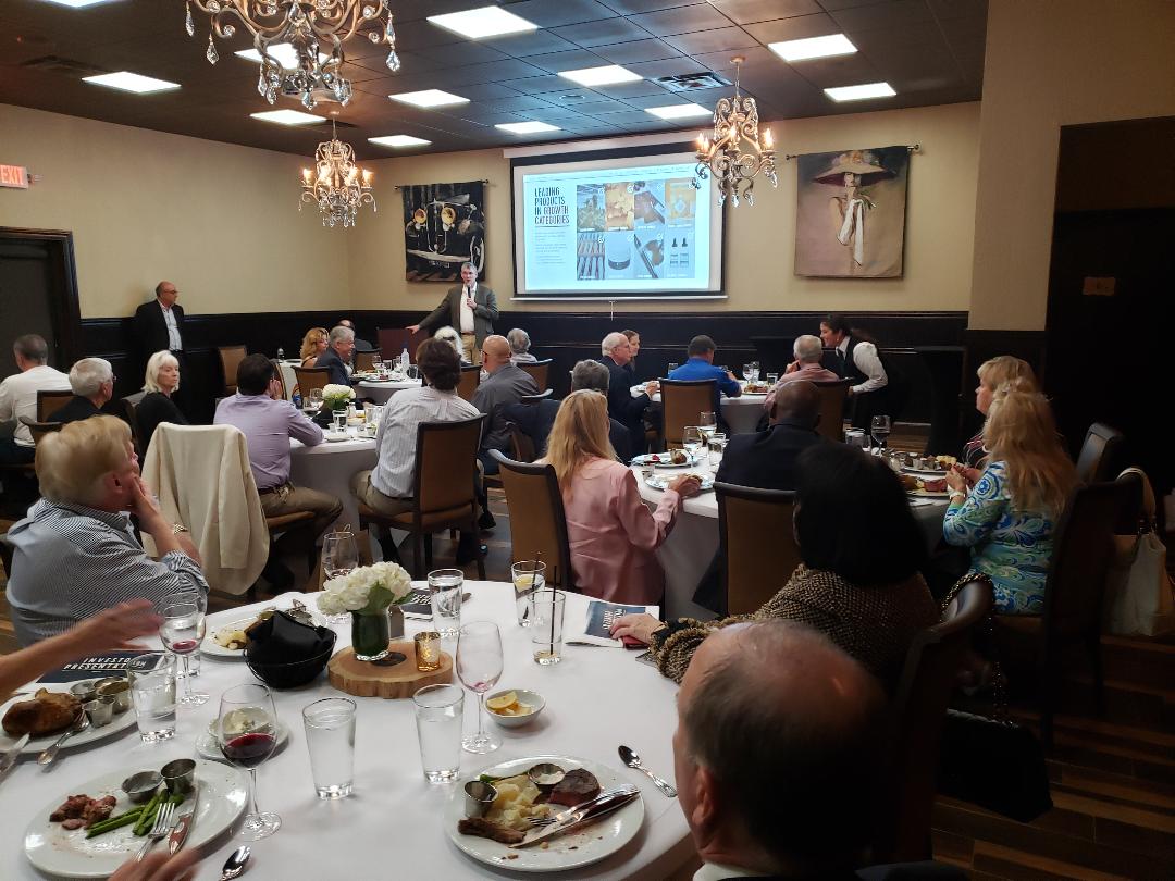 Guests seated beneath chandeliers watching a product presentation during dinner
