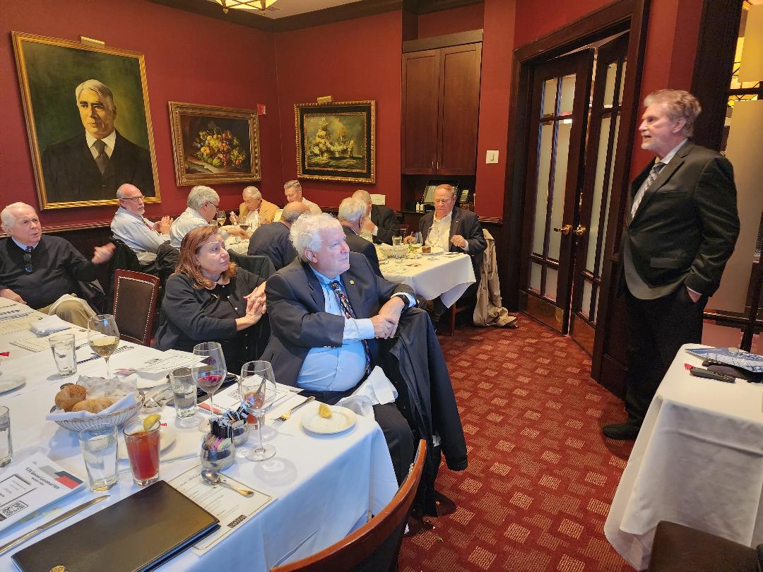 A presenter standing at the door of a red-walled private dining room addressing guests