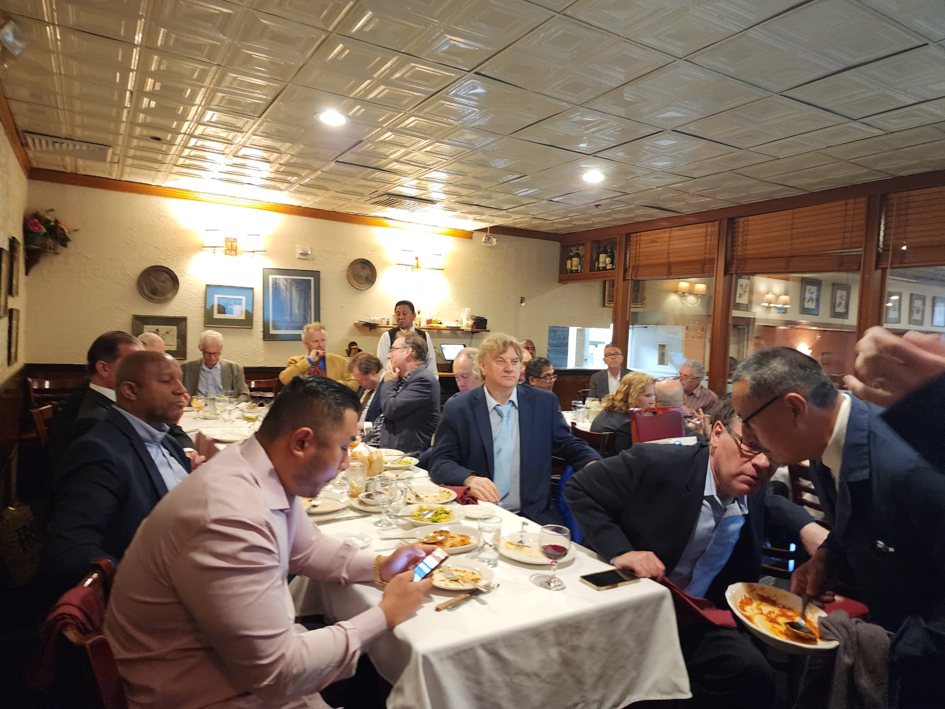 Guests at a long table in a classic tin-ceilinged restaurant during a meeting