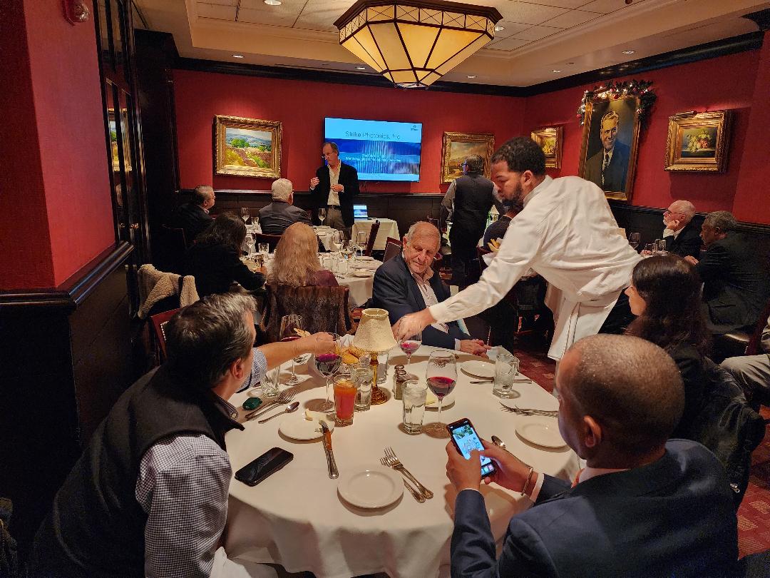A presentation underway in a red-walled steakhouse dining room as dinner is served